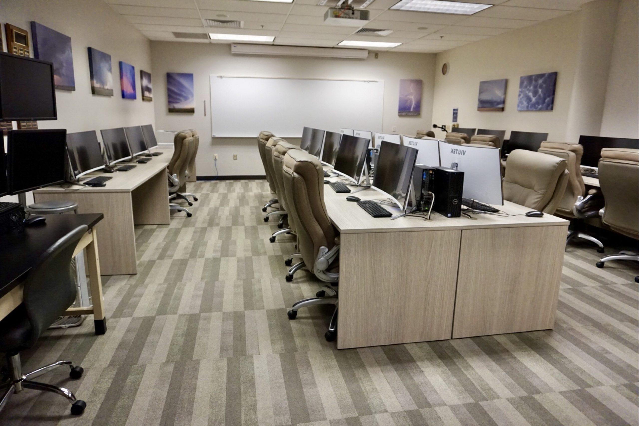 Several desks, computers, and monitors in the meteorology computer lab as well as canvas art on the walls with weather photos on them