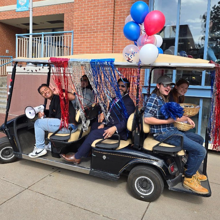 Golf cart full of voter engagement students with red, white, and blue balloons and fringe