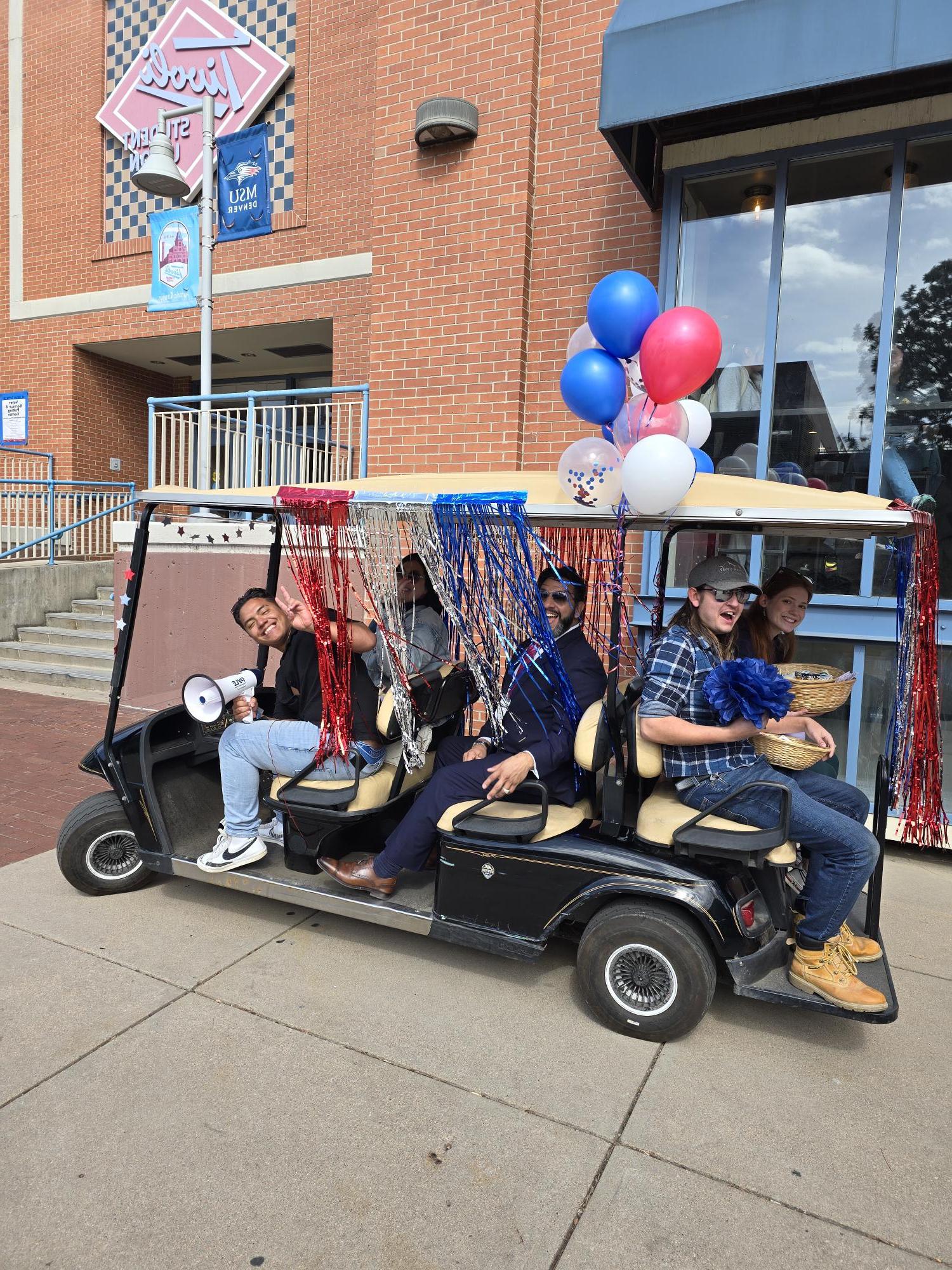 Golf cart full of voter engagement students with red, white, and blue balloons and fringe