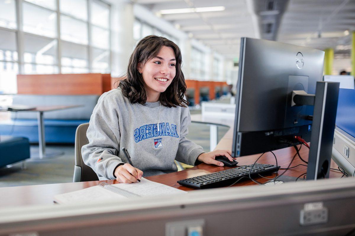 MSU Denver student, Abrianna Mangiamele, uses a computer while writing in a notebook